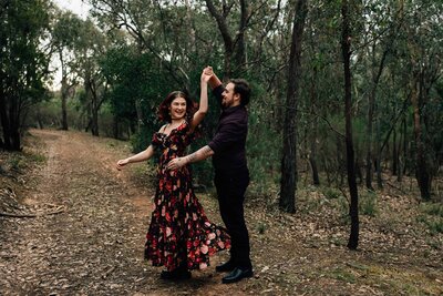 Man spinning woman in floral dress around outside in bush, dancing during a couples photography session, And So I Don't Forget Photography
