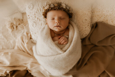 Photo of a baby sleeping all wrapped up in a pretty cloth with a flower crown.