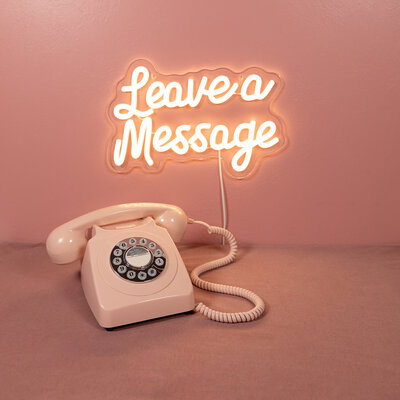Pink audio guestbook telephone on a pink background with  neon leave a message sign