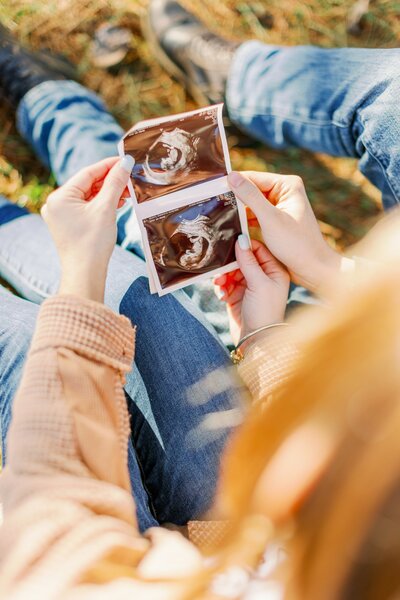 a man and woman smiling while holding a sonogram and baby shoes