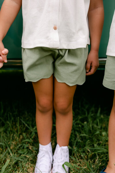 A little girl wearing a white shirt and green scalloped shorts back to school