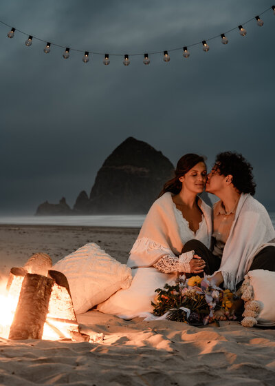 a couple snuggles up in front of a bonfire during their Oregon coast elopement.