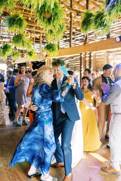 The groom and his mother dance during the reception under the plants in the barn of Paint Rock Farm in North Carolina, by destination photographer My Sun and Stars Co.
