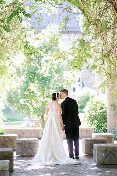 bride and groom kissing while standing under trees