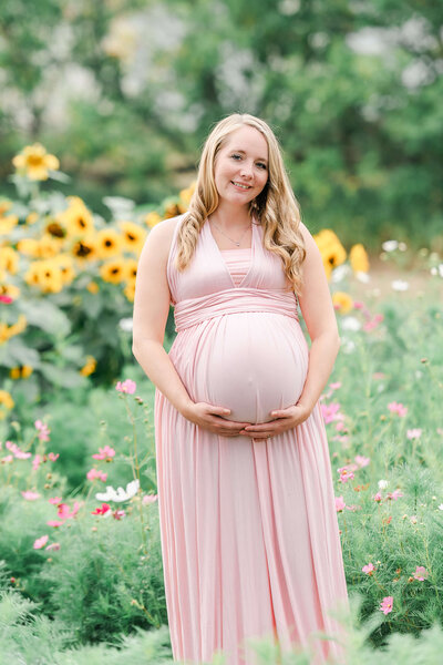 An expecting Edmonton mama wearing a pink Sew Trendy dress from Cynthia Priest Photography's client closet in a sunflower field