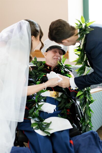 A newlywed couple leaning down with their arms around a grandparent in a wheelchair 