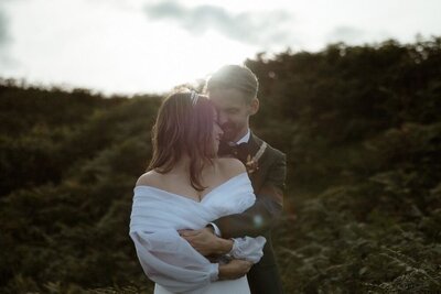 A couple hug during golden hour, surrounded by fern at the end of their Glencoe elopement in the Scottish Highlands