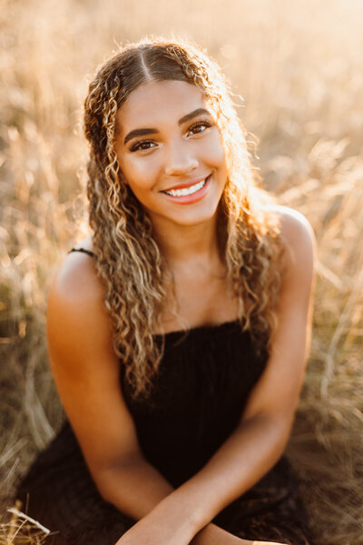 Close up portrait of a girl in a black dress sitting in a field
