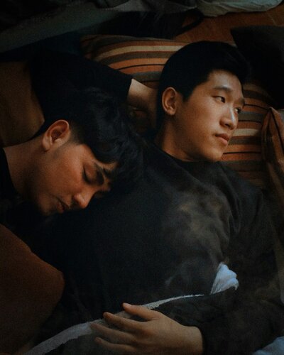 two men laying on bed laying on one another