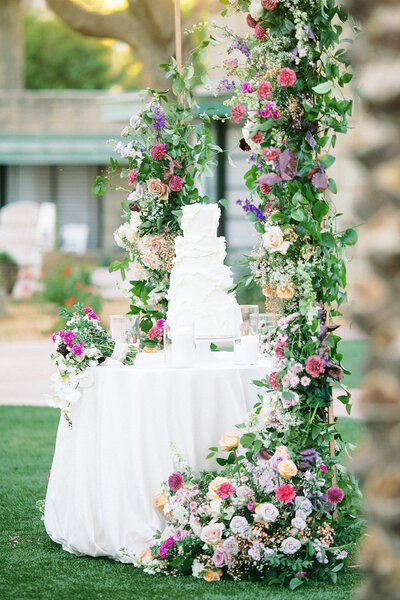 white tiered wedding cake surrounded with colorful floral arrangements