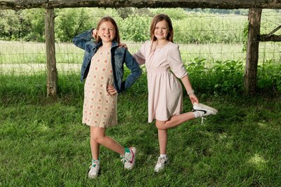 Two young girls on a farm psoing with one leg kicked up and hands on their hips.