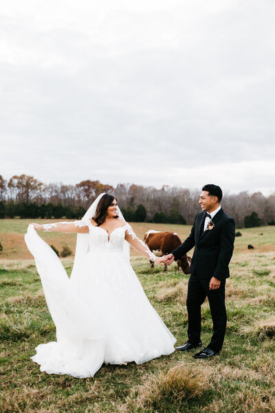 bride holding her dress out to the side as she dances with her groom is a field full of horses at a Charlottesville wedding venues