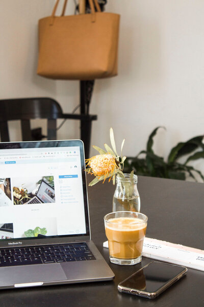 Laptop, coffee, and phone on a desk with a flower vase