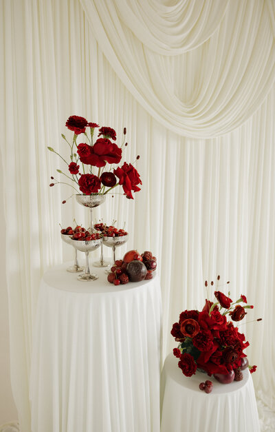 Crimson red florals and fruit styled in front of ivory elegant draping 