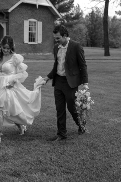 Groom gently holding the bride’s dress as they walk together on their wedding day, a sweet candid moment filled with care and connection.