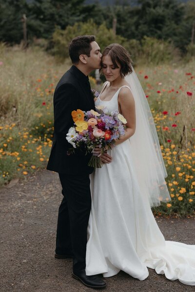 A bride holds her bouquet and the groom kisses her, representing a example of work in the florist portfolio.