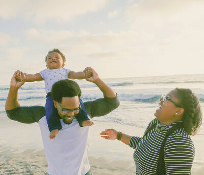 A young family looking at each other and smiling at the beach with the ocean in the background