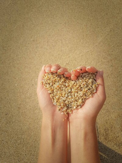 Hands holding heart-shaped sand on the beach, symbolizing care, nurturing, and the supportive approach of Pacific Kids Occupational Therapy.