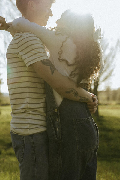 A candid engagement photo of a couple embracing each other during golden hour in Holland, Michigan.