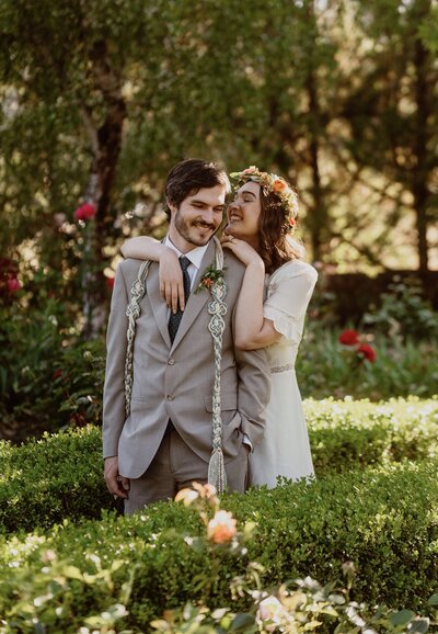 Grinning bride holding up her hand to display her new wedding band to her husband as they sip wine in the sun at The Madrones in Anderson Valley