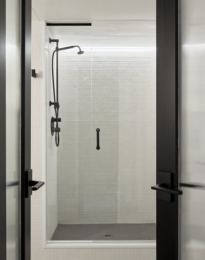 A minimalistic walk-in shower with grey tiling, black accents, and a sliding glass door.
