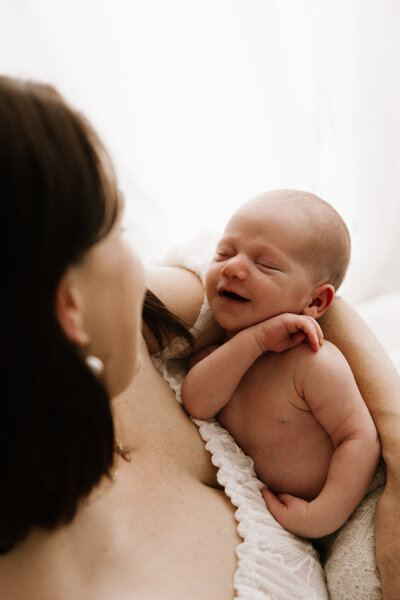 Newborn baby smiling in mother’s arms during soft, natural light photography session in Southwest Sydney studio