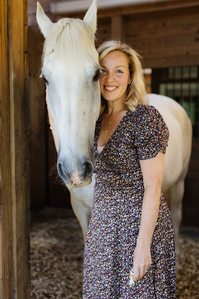 Founder of Peace Horse Collective standing beside her white horse in a warm, natural setting, captured in a soft, organic style that reflects the brand’s calm, earthy aesthetic.