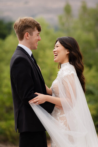 couple laughing and smiling at each other during their adventure session on a mountain top