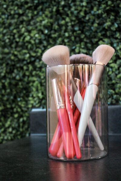 Makeup brushes in a glass container in front of a grass wall