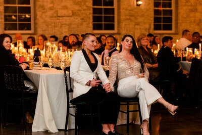 couple seated hand-in-hand, attentively listening to a loved one's speech at Grbic Events, a unique wedding venue in St. Louis
