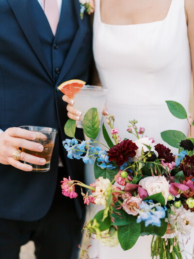 Close up of bride and groom holding a colorful bouquet and drinks