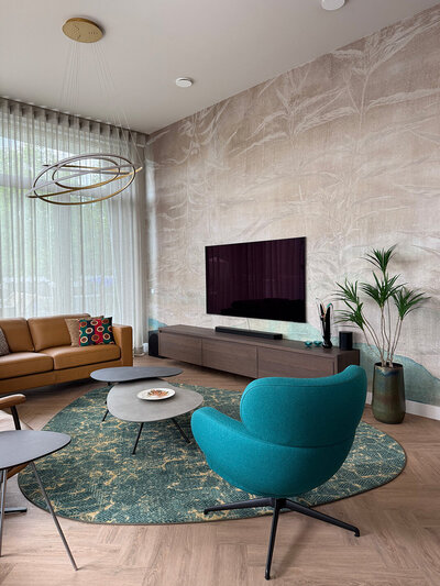 Interieur met ronde groene fauteuil, organische salontafels en modern behang in een lichte woonkamer