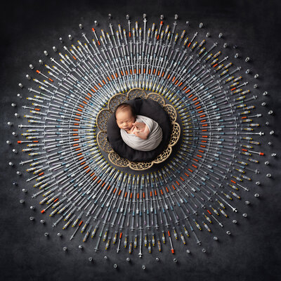 Newborn baby swaddled in neutral tones surrounded by hundreds of IVF syringes arranged in a circular rainbow pattern, celebrating the fertility journey with Dallas newborn photography studio specializing in newborn pictures and baby photography.