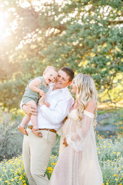 Family of three stands and playfully interacts playfully in a flower field, photography from Bay area photographer Light Livin Photography