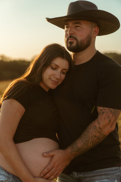 Rustic maternity couple session in a Tampa field at golden hour, featuring a tender embrace and hands on her baby bump.