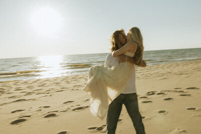 A blurry photo of a man holding his fiancée in his arms and kissing her at the beach on Lake Michigan.