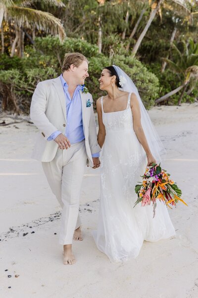 Happy bride and groom walking on white sand beach