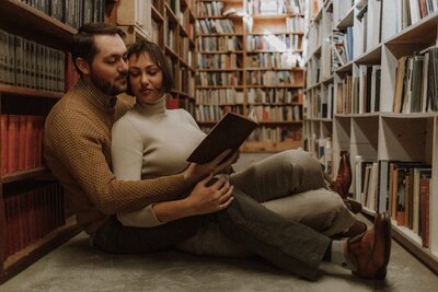 Couple snuggles up and reads a book sitting on the floor of a book store.