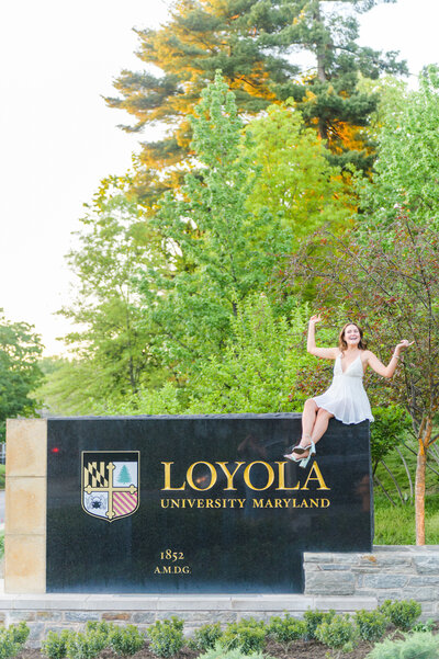 Loyola Grad smiles on Loyola University Maryland sign during sunset graduation session by Cait Kramer Photography
