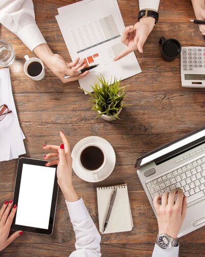 GROUP OF PEOPLE WORKING ON LAPTOPS AND TABLETS ON A TABLE