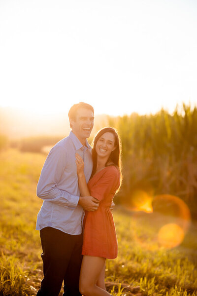 Happy engagement couple in the green field of grass under the sun