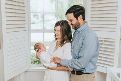 Mom and dad hold newborn baby girl by window in nursery