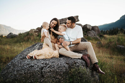 Family of parents, a baby, and a toddler sitting on a big rock in the Columbia river gorge