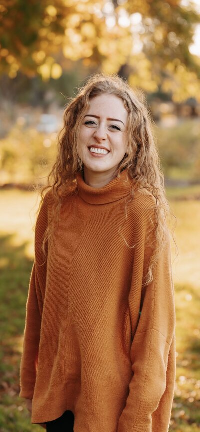 headshot of Mack smiling in an orange sweater