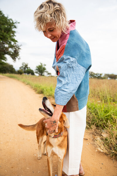 Sasha bending over to pet dog on dirt road on the farm