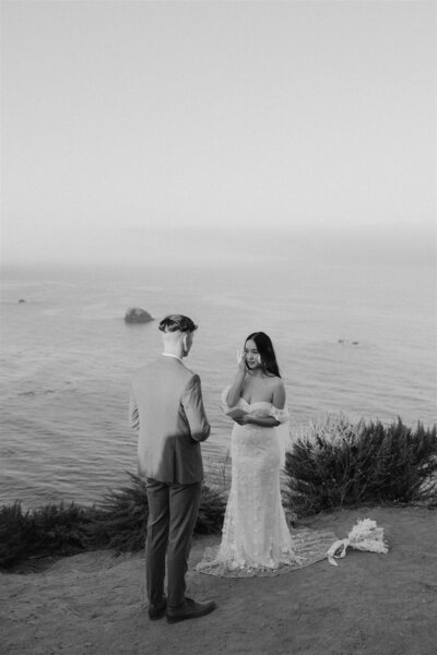 bride and groom saying vows on a rocky overlook on the ocean bride wiping tear
