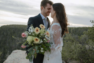 bride and groom kissing on mountain side with sin beaming behind them