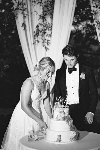 Black and white photo of bride and groom cutting their wedding cake beneath romantic draping | Ohio wedding photographer