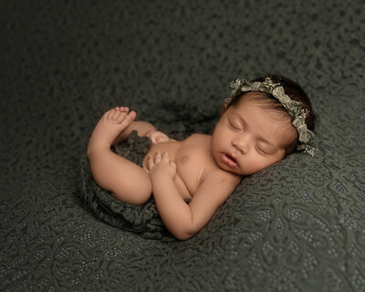 Newborn baby girl in floral headband peacefully posed on textured green backdrop during studio newborn session with Hello Photography in Austin, Texas.