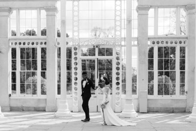 Black and white image of a bride and groom walking through  Syon Park wedding venue